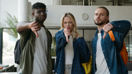 Three multiracial friends diversity students showing thumbs down negative dissatisfied bad dislikes...