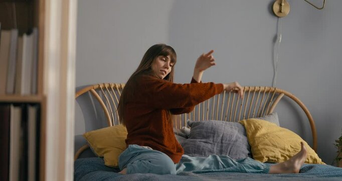 Girl in casual clothes improvises and dances on bed in cozy apartment in the morning. Improvised dance and body movement in the morning