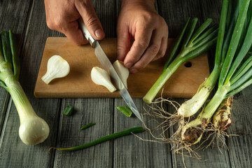 A pair of hands is trimming fresh green onions on a wooden cutting board. The kitchen exudes a warm atmosphere, making the food preparation inviting and homely