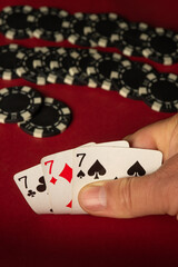 A player displays three sevens, indicating a strong hand in a friendly card game. Poker chips lie...