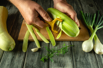 Hands use a peeler on a green vegetable marrow while surrounded by freshly cut scallions, garlic,...