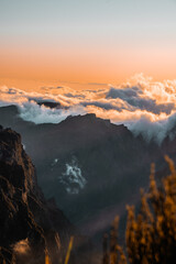 Sunset view of Pico do Arieiro mountain with vibrant orange sky and clouds behind the peak,...