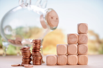 Stacked coins and wooden blocks beside piggy bank glass representing savings, financial growth, and...