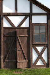 A fragment of the facade of a vintage wooden building: a plank entrance door with a bolt lock and a window in a brown wooden frame.