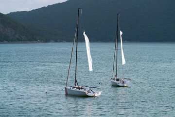 Two sports sailing yachts at anchor in the middle of Lake Abrau, surrounded by mountains.