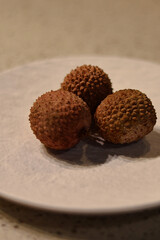 Fresh lychee fruits arranged on a white platter in natural light. Vibrant red shells and juicy...