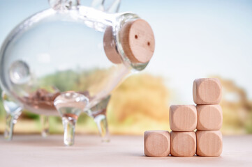 Stacked wooden blocks with transparent piggy bank alongside coins suggesting financial planning, growth, and investment with a neutral backdrop promoting savings