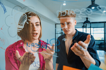 Couple of businesspeople discussing and brainstorming about solving marketing problem in front of glass board at business meeting by using mind map and sticky notes. Working together. Immaculate.