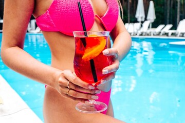 Cropped photo of slim young woman posing against swimming pool while holding cocktail. Relaxing...