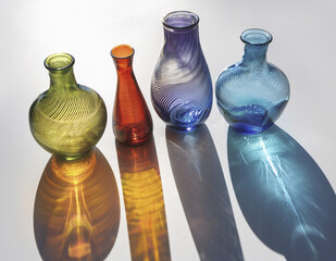 A group of colored glass vases casting rainbow shadows on a white floo