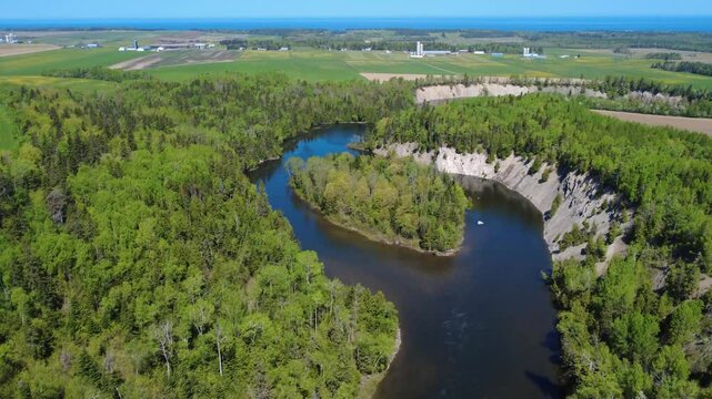 Aerial view showcasing a scenic river island nestled in a rock-cut gorge, flowing past lush woodlands and farmland along the Mitis River, Price, Quebec, Canada.