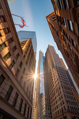 Looking up at skyscrapers in a city downtown with sunburst effect and the United States flag waving in the blue sky.