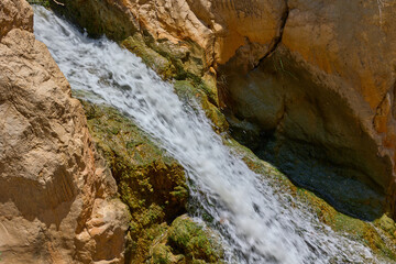 Small waterfall flowing over mossy rocks in a canyon on a bright sunny day