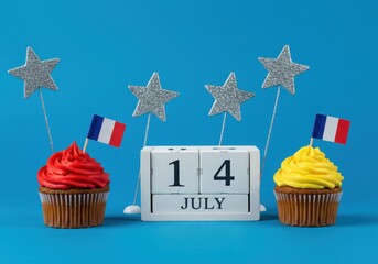 Two delicious cupcakes with red and yellow frosting sit beside a july 14th calendar, adorned with silver stars and french flags