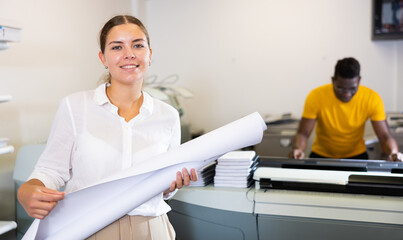 Obraz premium Portrait of friendly female employee of printing house with a stack of notebooks in her hands