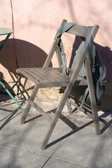 Wooden chair with hanging green backpack near cafe table, outdoor coffe break in spring or summer city. First warm days and open terraces on streets. Rest pause during walk