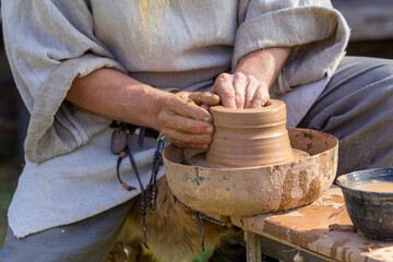 Close-up of a potter's hands skillfully shaping clay on a traditional kick wheel, demonstrating...