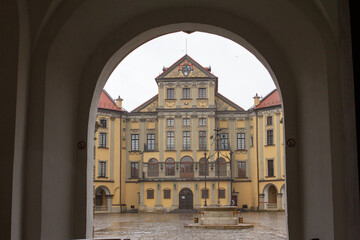 Obraz premium The grand Nesvizh Castle, a historical landmark, is viewed through a stone archway, showcasing its intricate Baroque architecture and central courtyard
