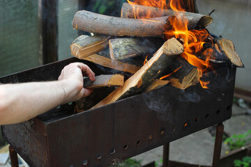 Hand puts wood into the fire. Man makes a fire. Make barbecue in the garden. Firewood is burning in...