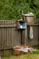 A rustic outdoor hand-washing station with a metal basin and toiletries, set against an old wooden...