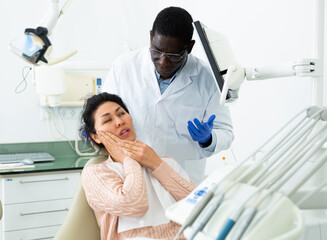 Woman patient who came to an appointment with a male dentist is sitting in a dental chair in the...