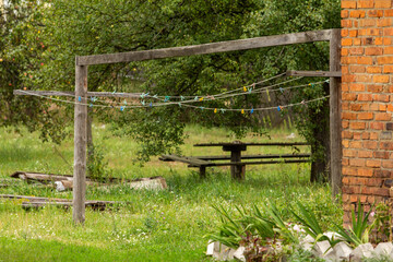 An outdoor wooden clothesline with colorful pegs, set in a rustic green backyard with a tree and...
