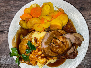 rustic veal roll roast with Polenta, corn porridge with gravy and carrots, traditional Swiss menu in plate on wood, top down view