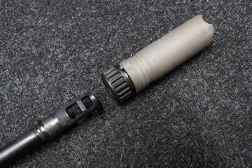 Close-up: installing or detaching a suppressor (sound moderator) on a rifle barrel's muzzle brake. Concept of tactical accessories and weapon modification.