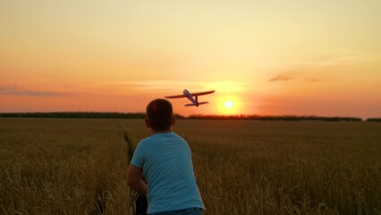 Dreaming boy throws toy airplane into flight child plays in wheat field sunset. Child dreams of fly travel. Child plays with toy airplane. Child boy wants to travel around world, sun sky. Slow motion
