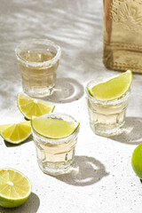 Refreshing tequila shots served with lime wedges on a textured surface, showcasing vibrant colors...