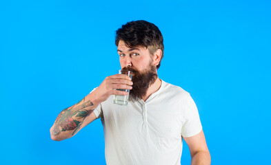 Handsome bearded man drinking glass of fresh water. Attractive man in casual white t-shirt drinking...