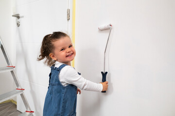 Smilling child with curly hair painting a white wall in the apartment . 