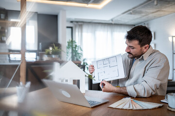 Architect designing house interior using laptop and showing blueprint to client online
