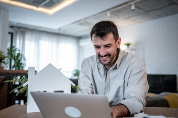 Architect smiling and working on laptop with house model on table