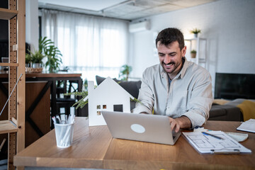 Architect working from home on a laptop with house model and plans visible