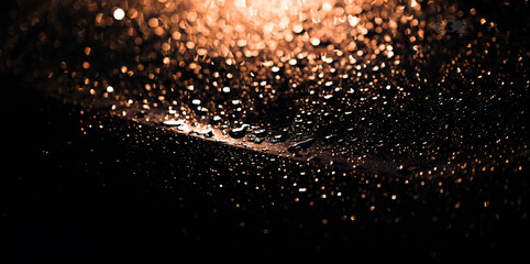 Rain drops on a black car hood at night, illuminated by warm street light. Shallow depth of field...