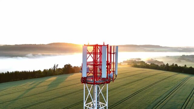 Aerial drone footage of a telecommunication tower enveloped in morning fog at sunrise. Soft golden light, misty atmosphere, calm nature, technology blending with environment, peaceful and inspiring ur