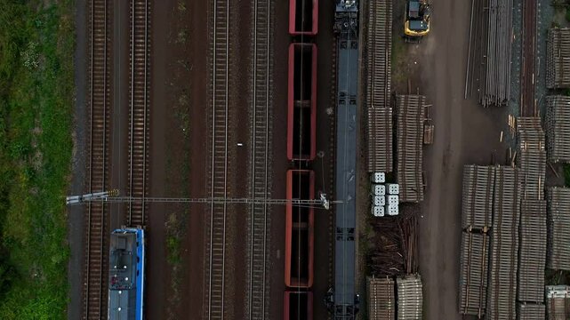 Aerial drone footage of a moving freight train traveling through diverse landscapes. The powerful locomotive pulls cargo cars along winding tracks, showcasing industrial transport and logistics effici