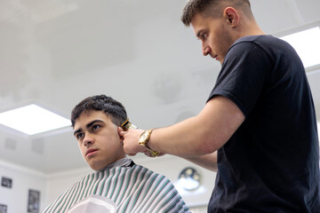 Professional Barber Giving a Haircut to a Young Client with an Electric Trimmer. Young Male Barber...