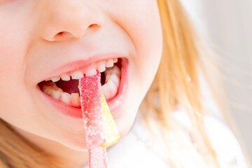 blonde girl 5 years old girl eating sweet gelatin candies, looking forward to enjoying favorite...