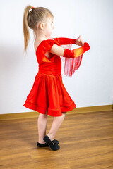 charming 5-year-old blonde girl, dancer in vibrant red dress performs Latin dance steps, showing...