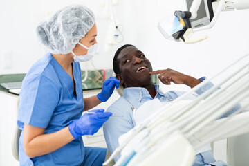African american patient talking to female dentist and complaining about toothache at dental clinic...