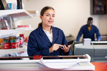 Cheerful young female specialist in uniform calculates the cost of notepads and sheets in the...