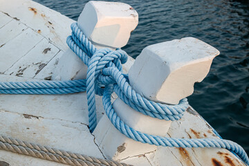 Close-up of blue mooring ropes tied in a nautical knot around white wooden bollards on a vintage...
