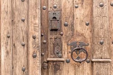 Closeup of an old antique wooden door with ornate metal handle and weathered surface medieval building entrance gate detail, historical church castle building, rustic textured planks steel studs