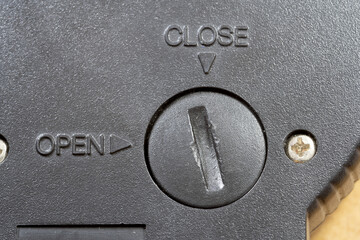 Closeup of a simple closed electronic device battery compartment cover with open and close arrow indicators showing screw cap mechanism for inserting batteries, macro detail of black plastic surface