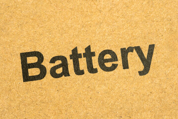 Closeup of black printed word “battery” on a brown cardboard box surface, macro detail view of...