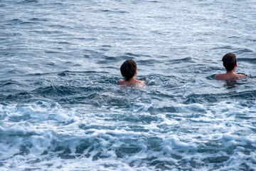 Two young children, teenagers boys splash and play in sea, ocean waves on sunny summer day, family...