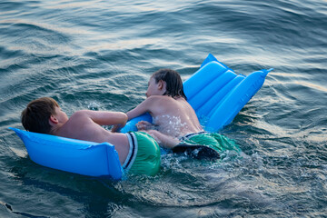 Two children swimming in sea, adrift on blue inflatable raft, accident in open water, inflatable...