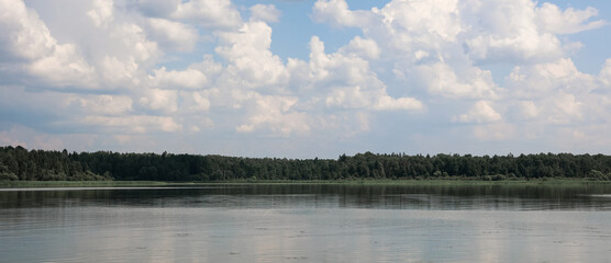 Tranquil lake reflecting a dense green forest under a cloudy sky, creating a serene and peaceful...